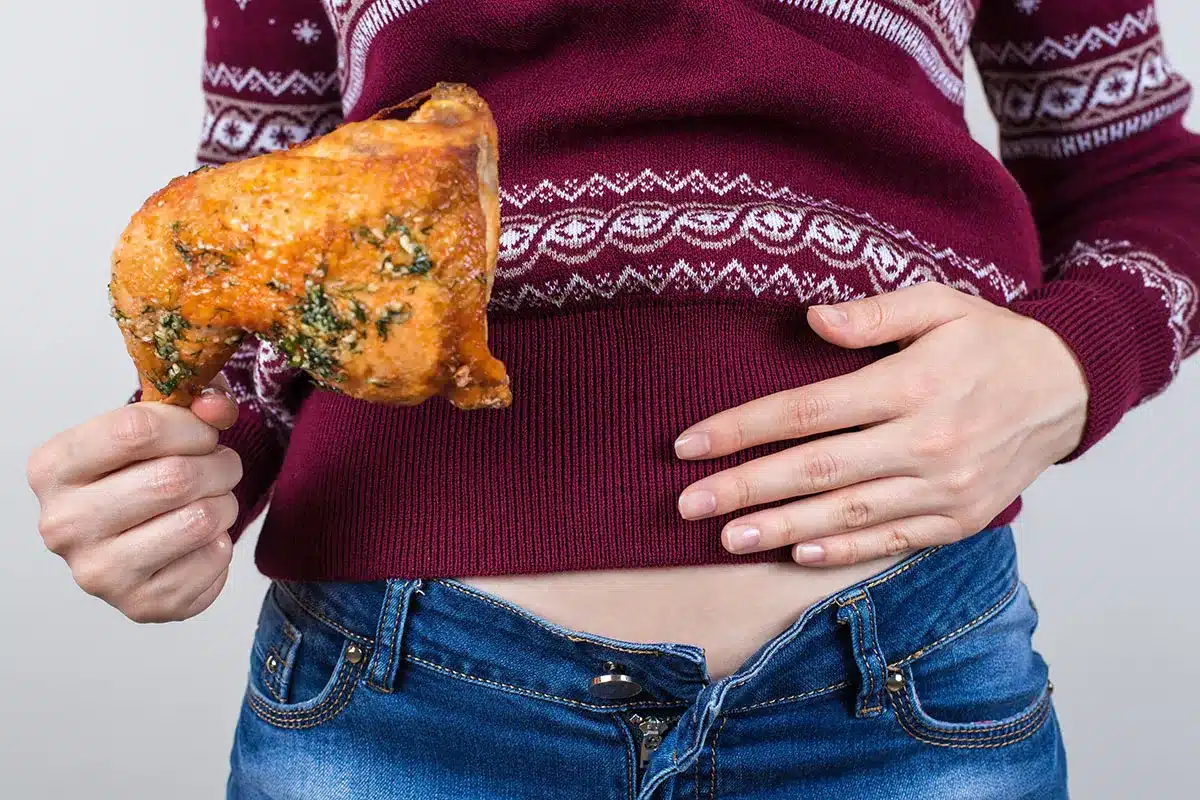 Woman holding a roasted chicken leg near her stomach.