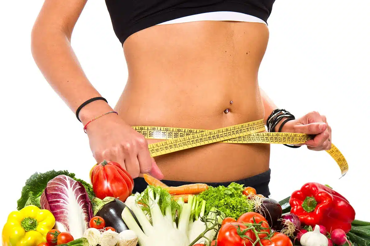 Woman measuring waist with vegetables.