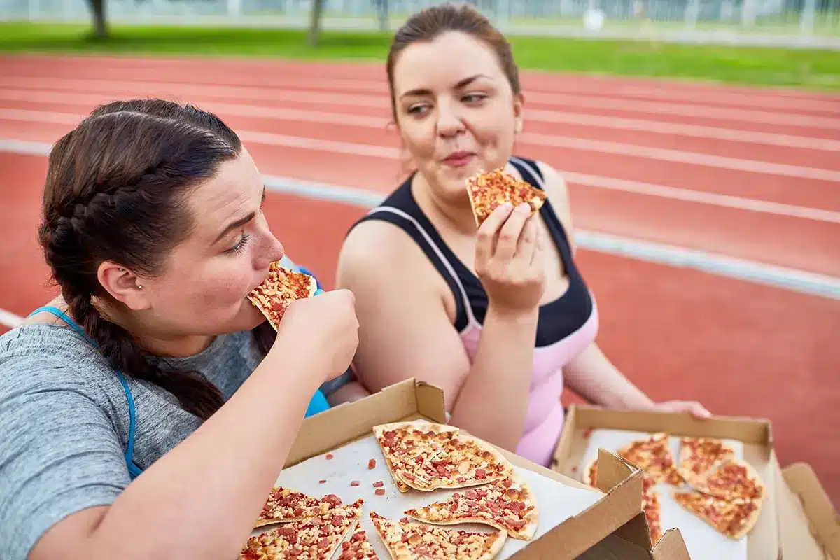 Two plus-size women enjoying pizza.