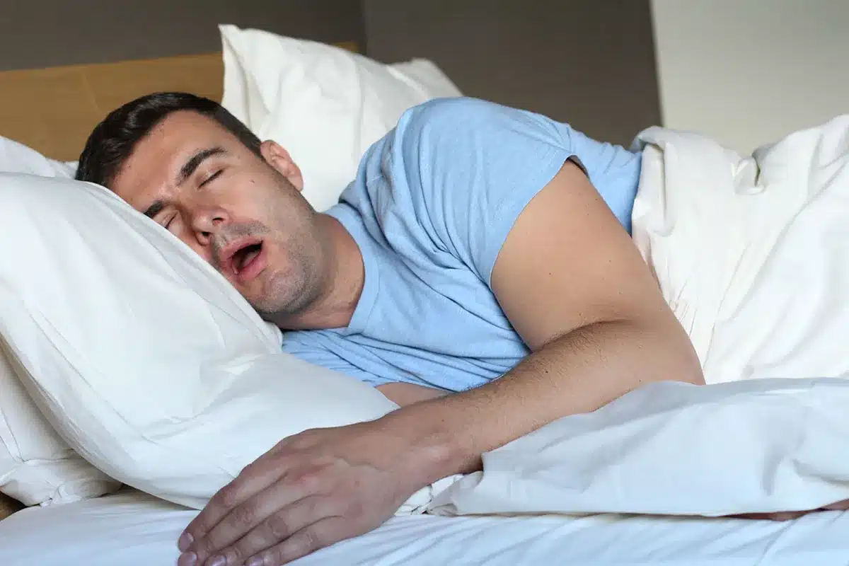 Man asleep in bed, mouth open.
