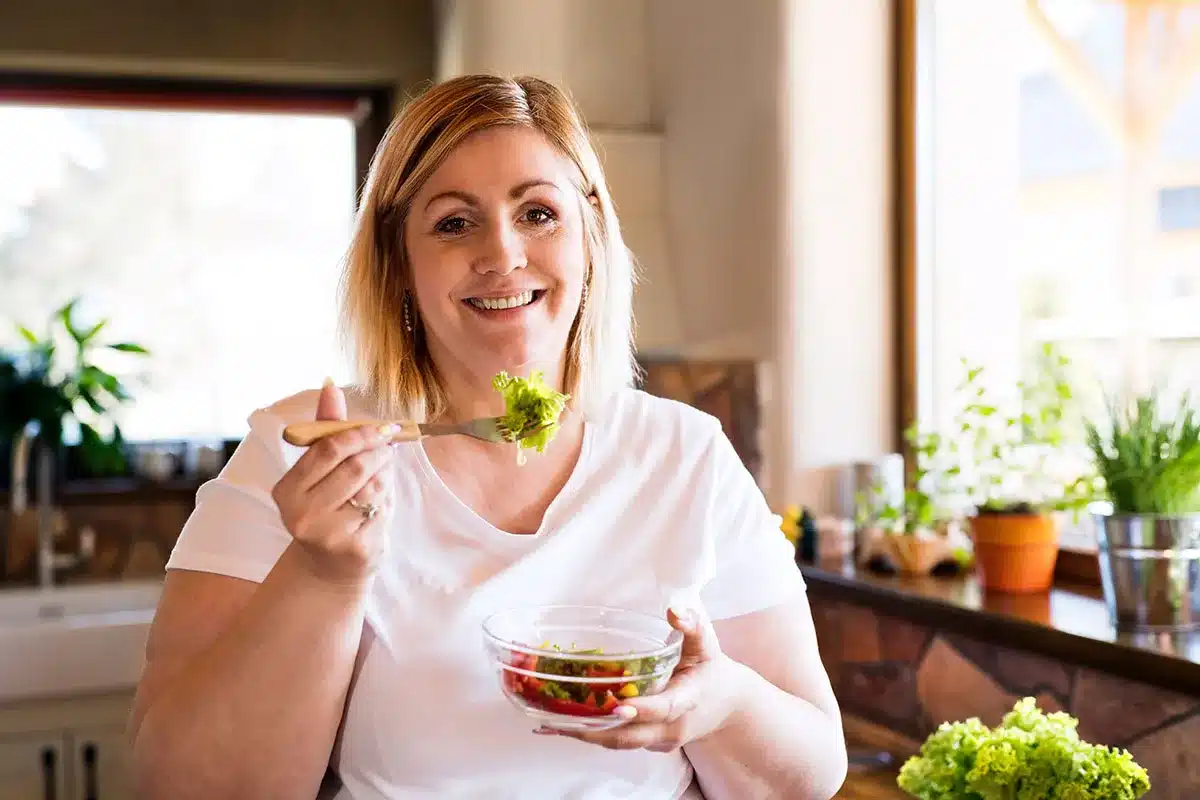 Woman eating a salad and smiling.