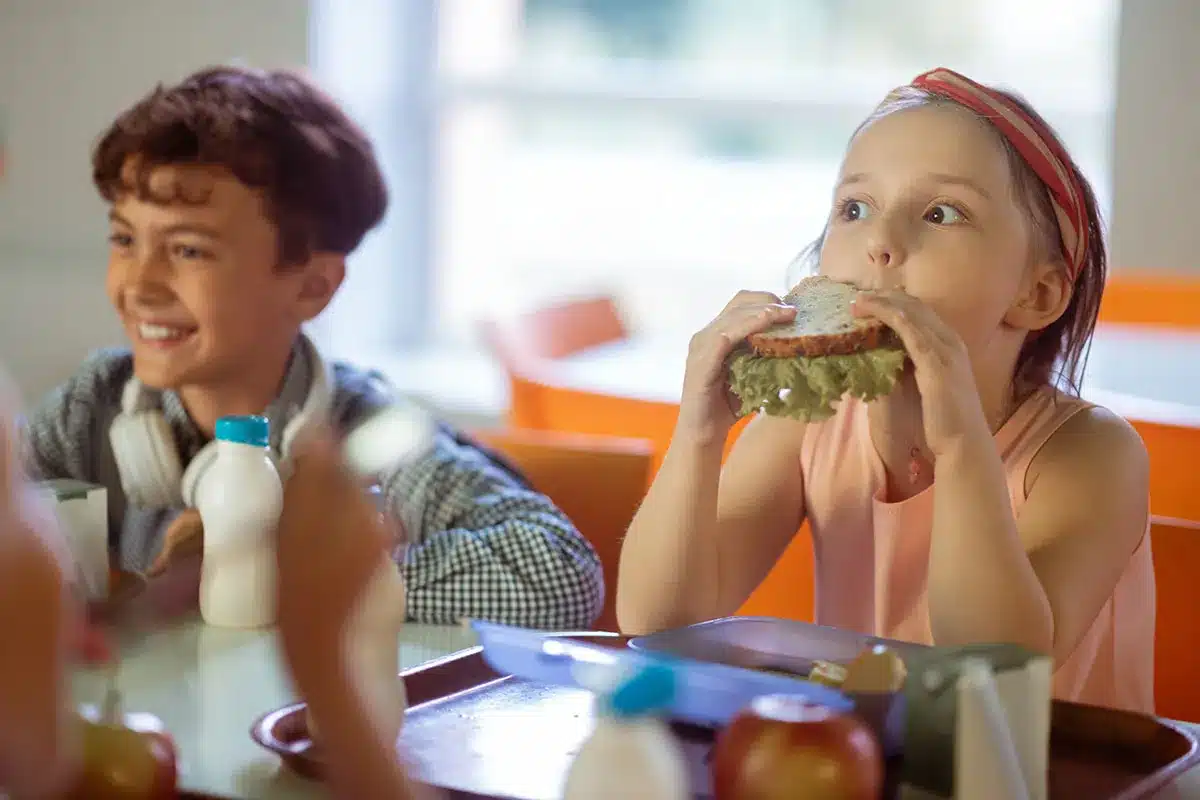 Girl eating a sandwich in school cafeteria.