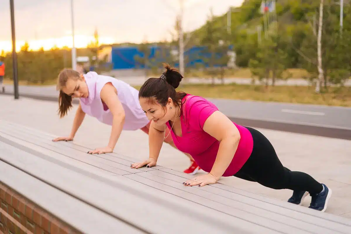 Two women doing push-ups outdoors.
