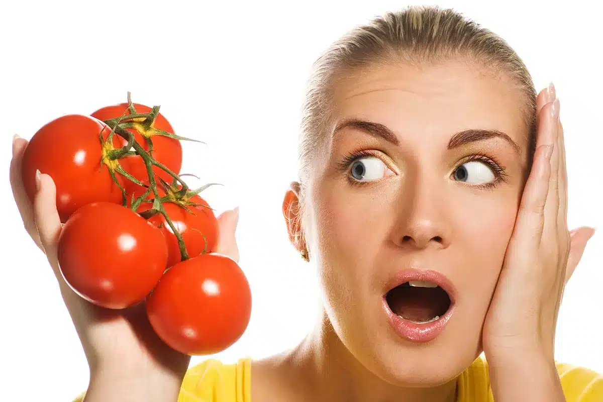 Woman with surprised expression holding tomatoes.