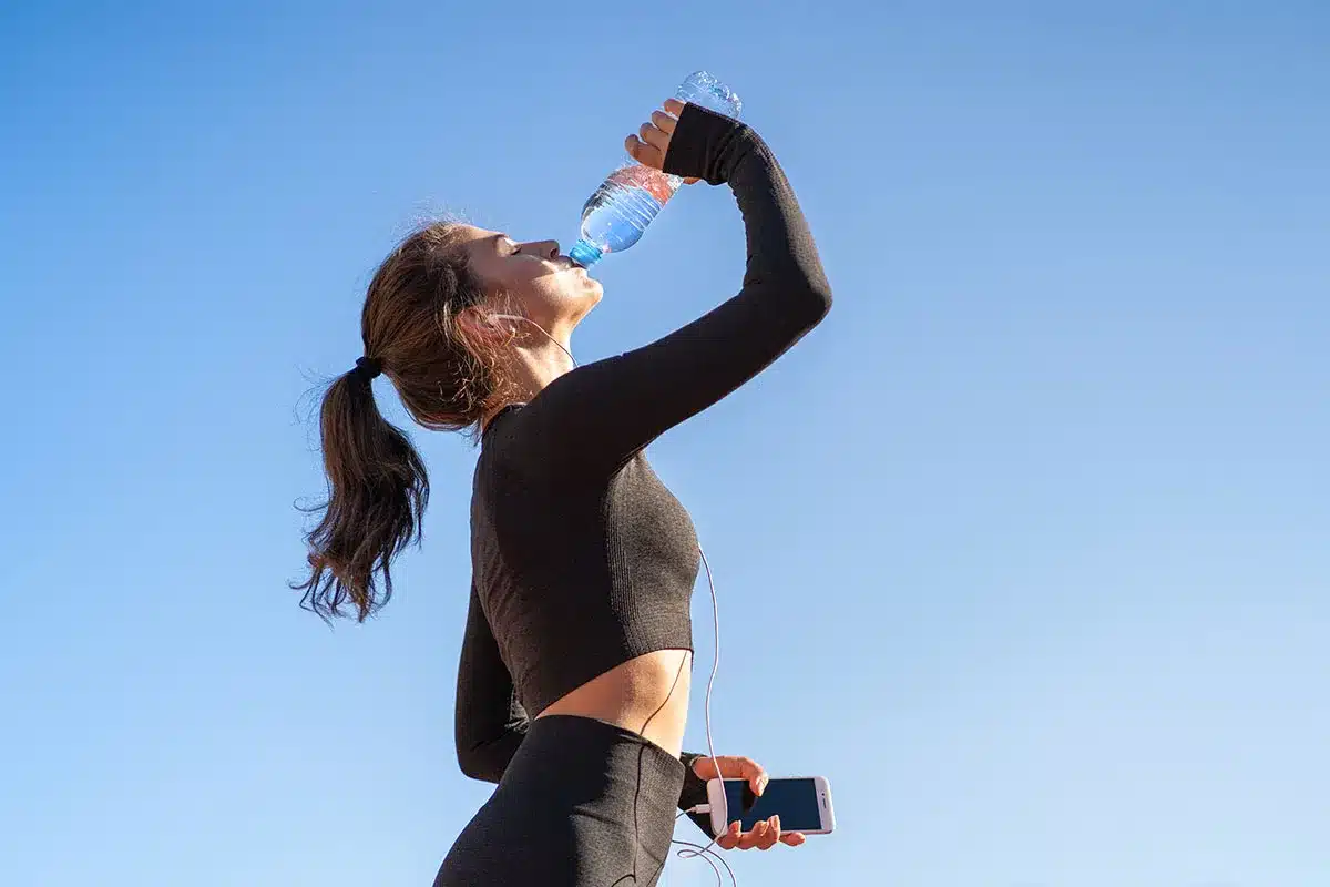 A woman holding a water bottle outdoors under the summer sky.