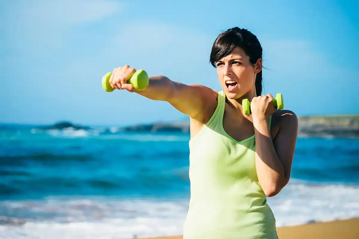 Woman exercising with dumbbells on beach.