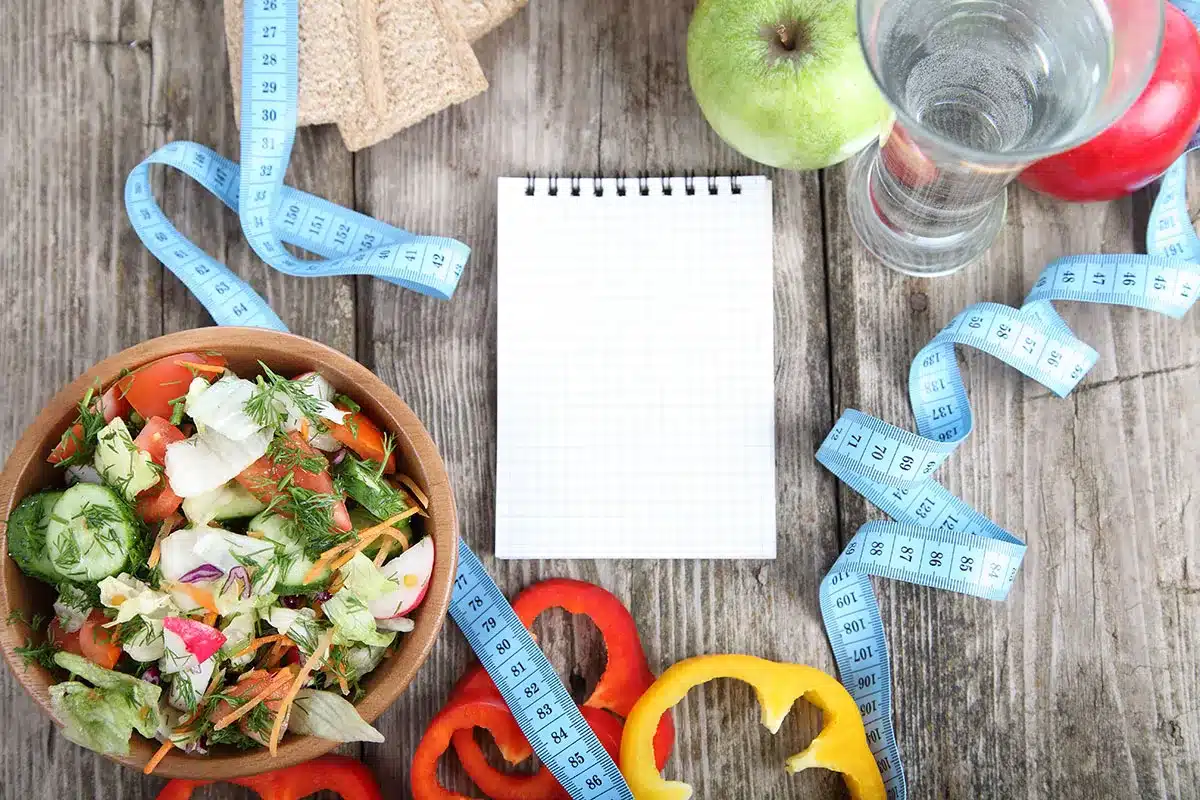 Healthy salad, measuring tape, and notepad for diet plan.