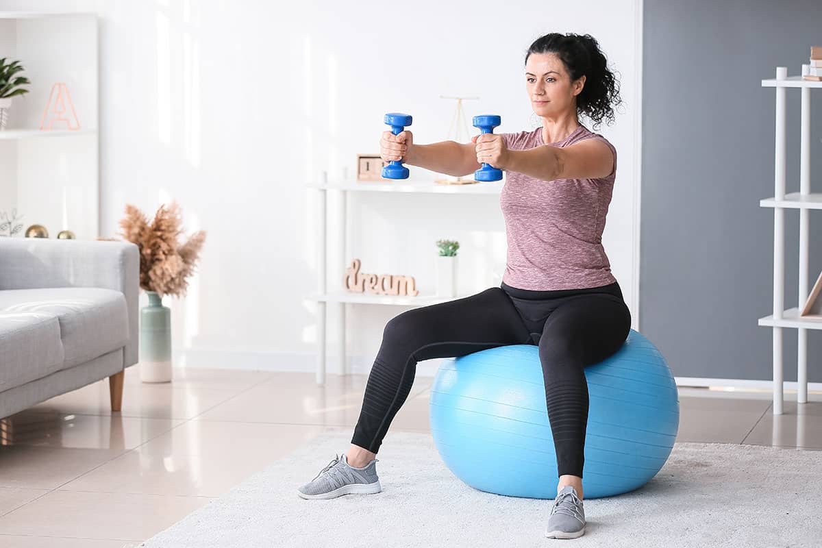 Woman doing dumbbell exercises on fitness ball.