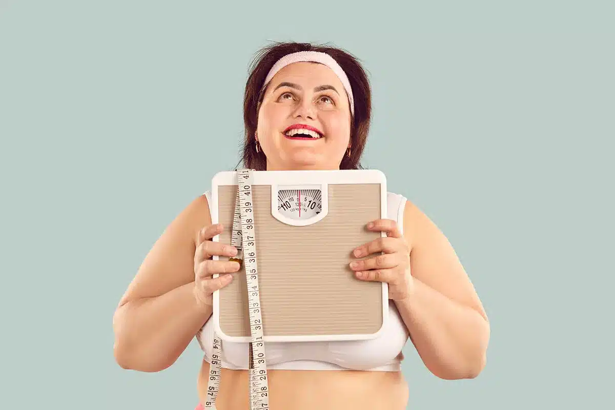 Happy plus-size woman holding scale and tape measure.