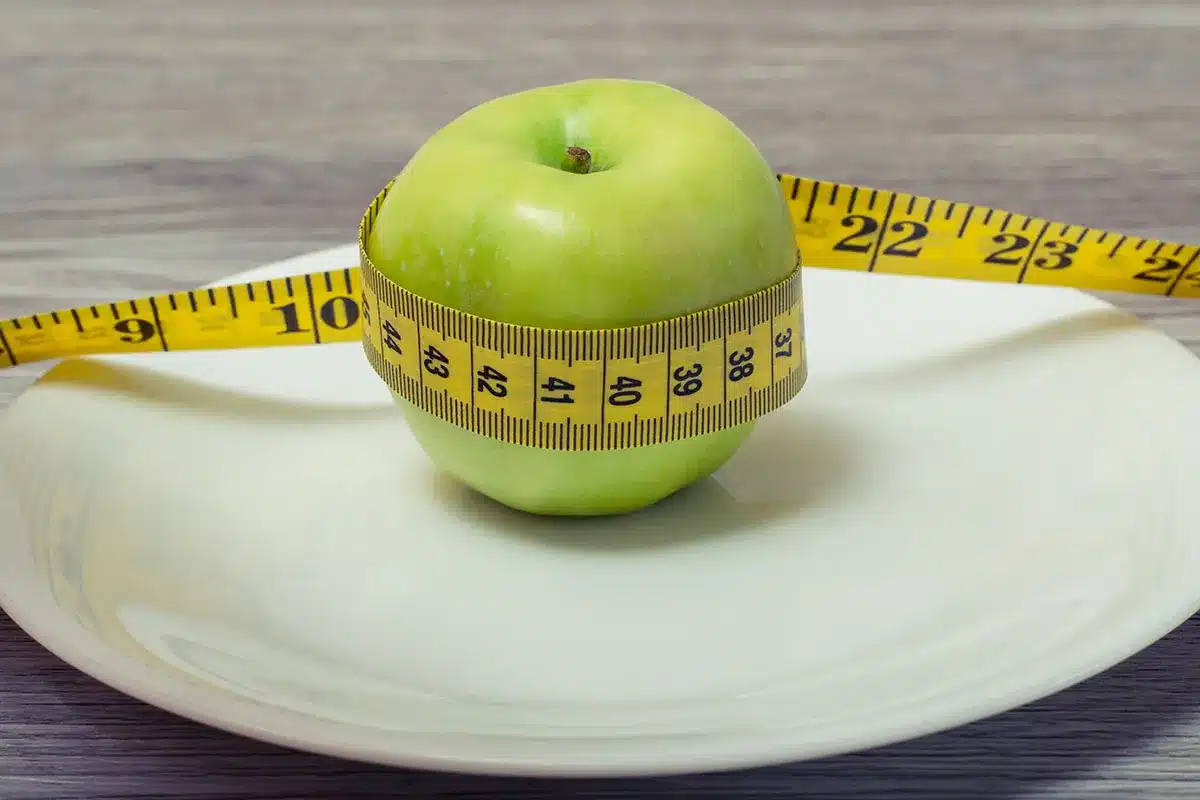Green apple with measuring tape on plate.