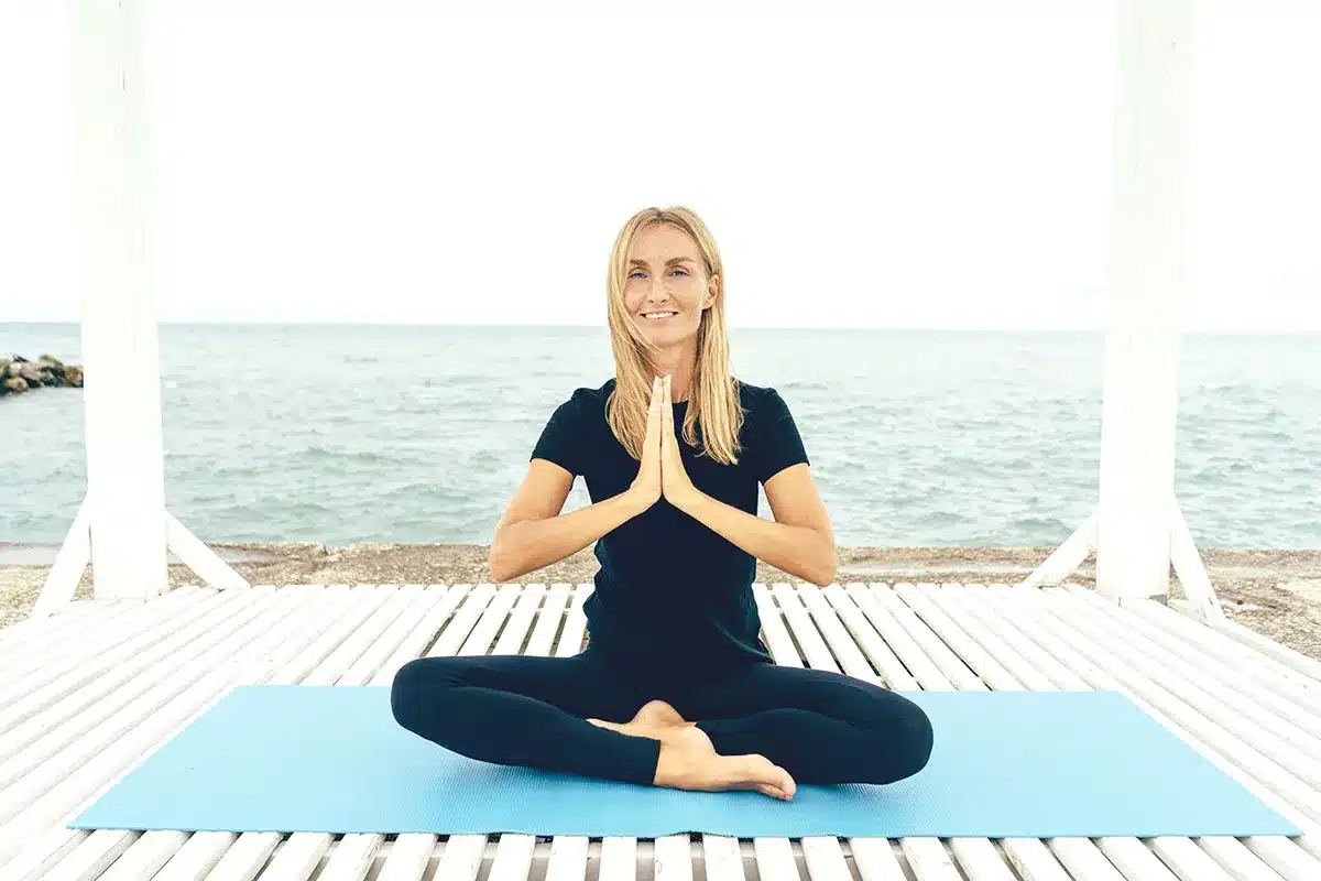Woman meditating on beach, ocean view.