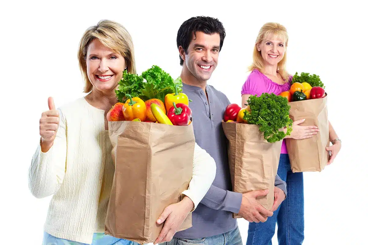 Three people holding grocery bags of produce.