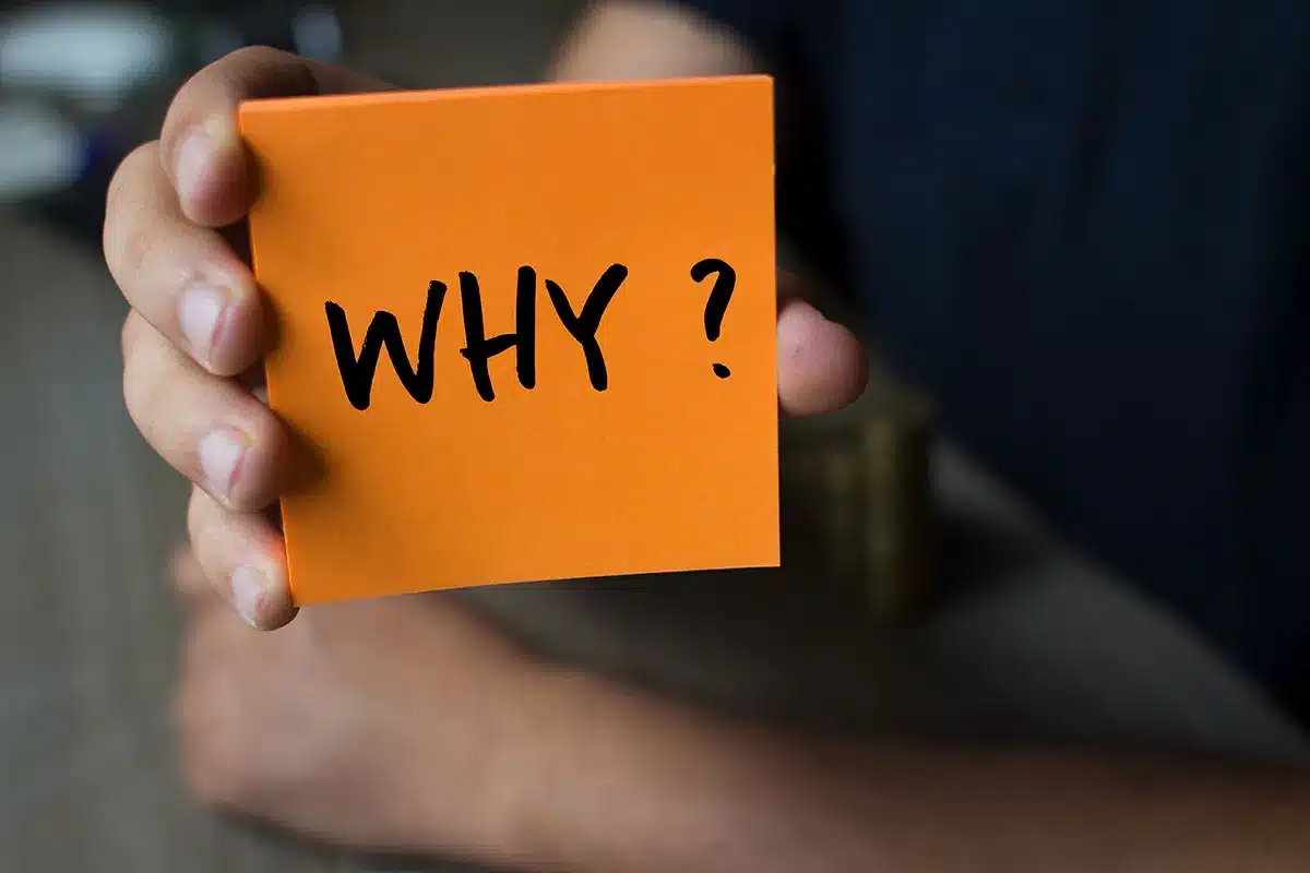 Hand holding a note that says "Why?"