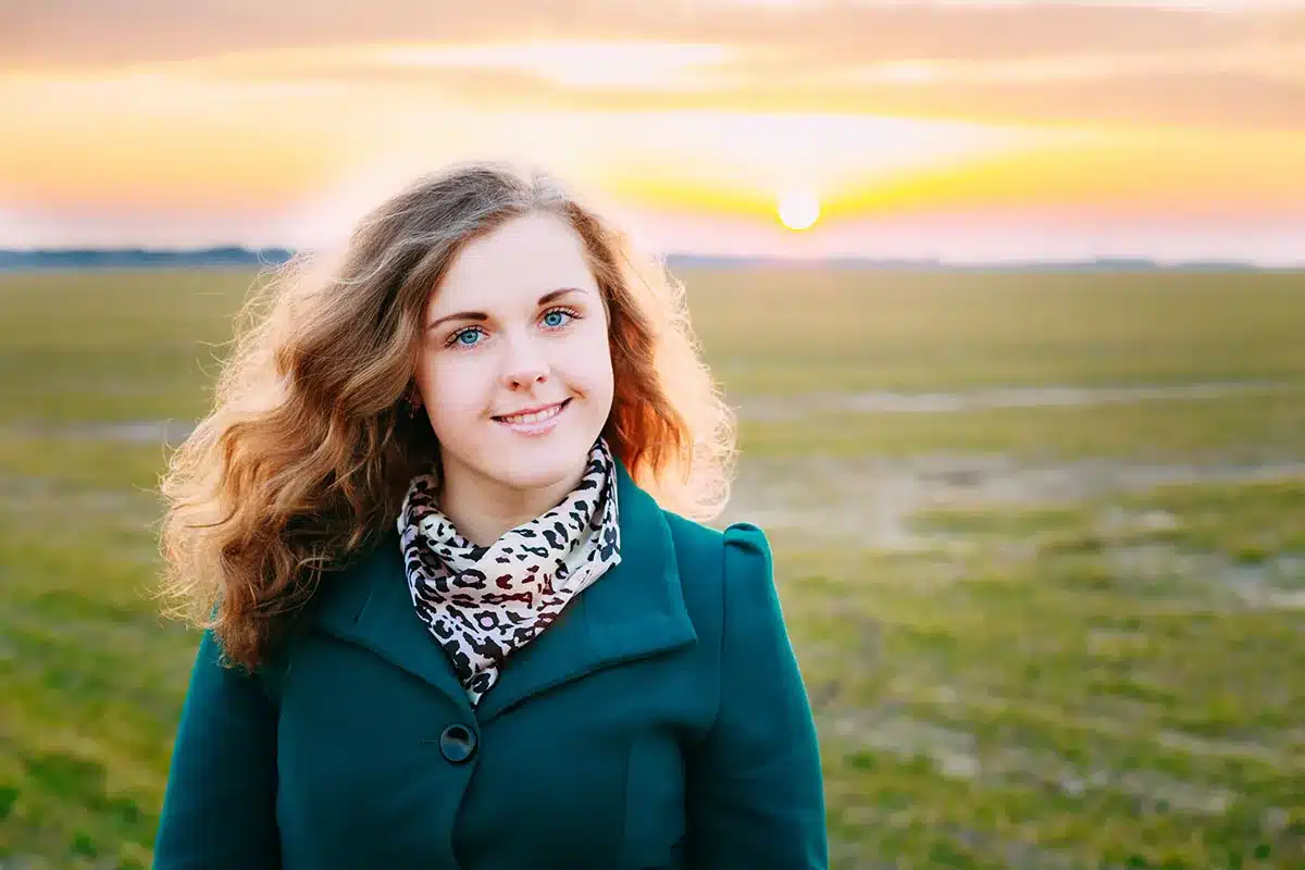 Smiling woman in green coat, sunset background.