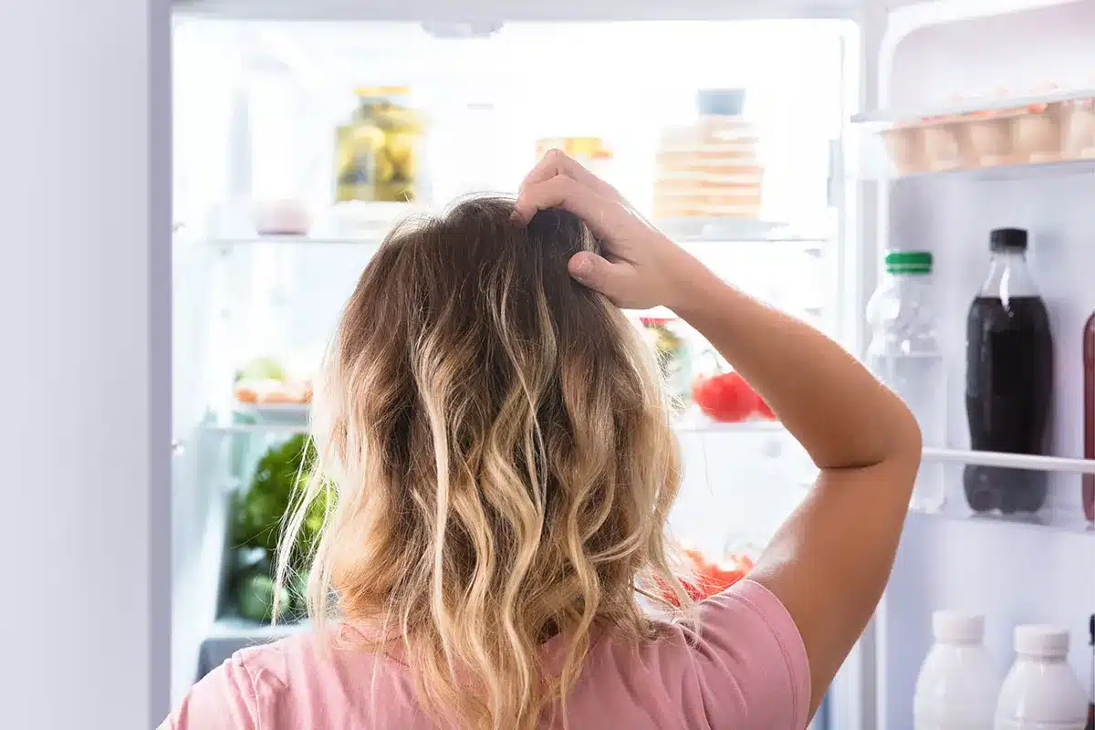 Woman looking confused at a refrigerator.