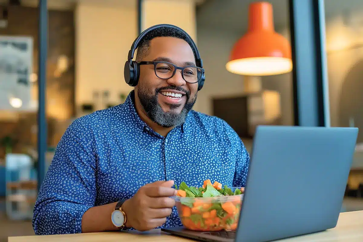 Man with headphones eating salad, laptop.