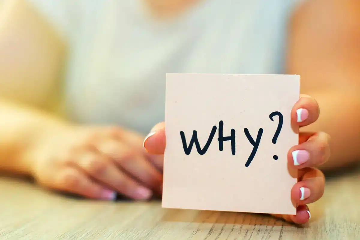 Woman holding a card with "Why?" written on it.