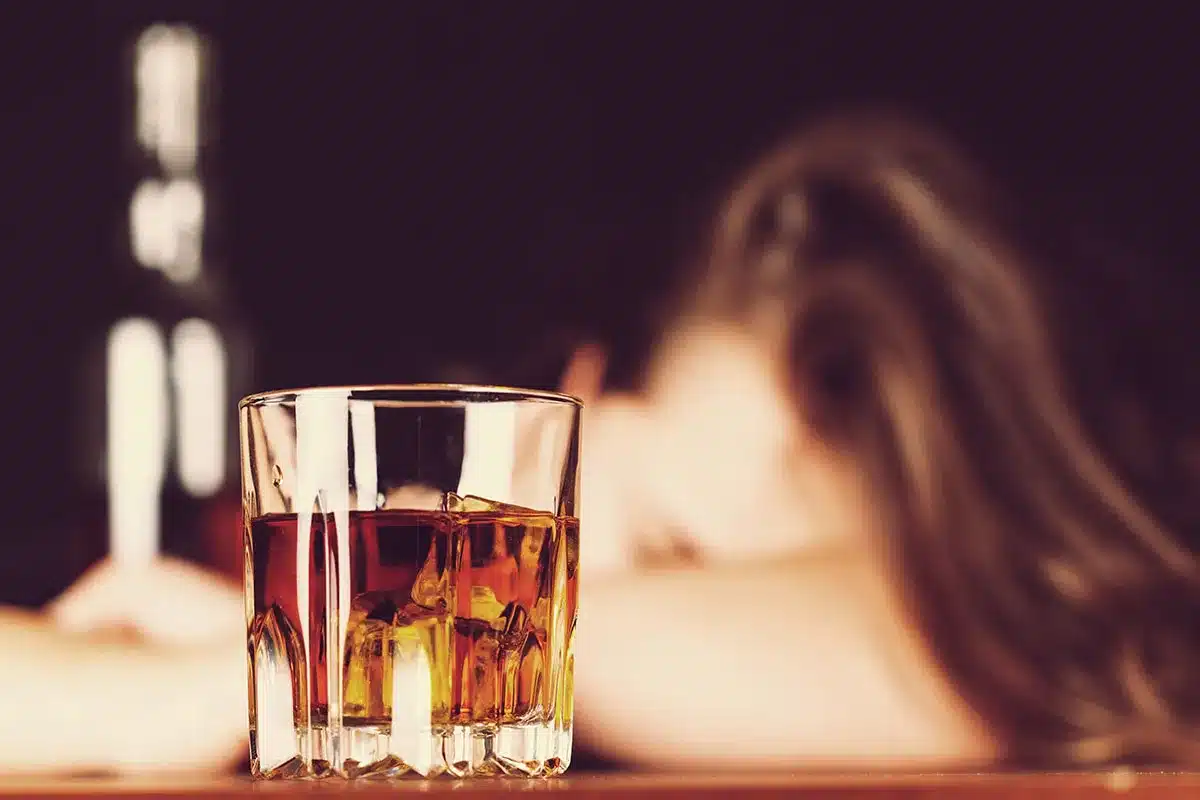 Glass of whiskey with woman in background.