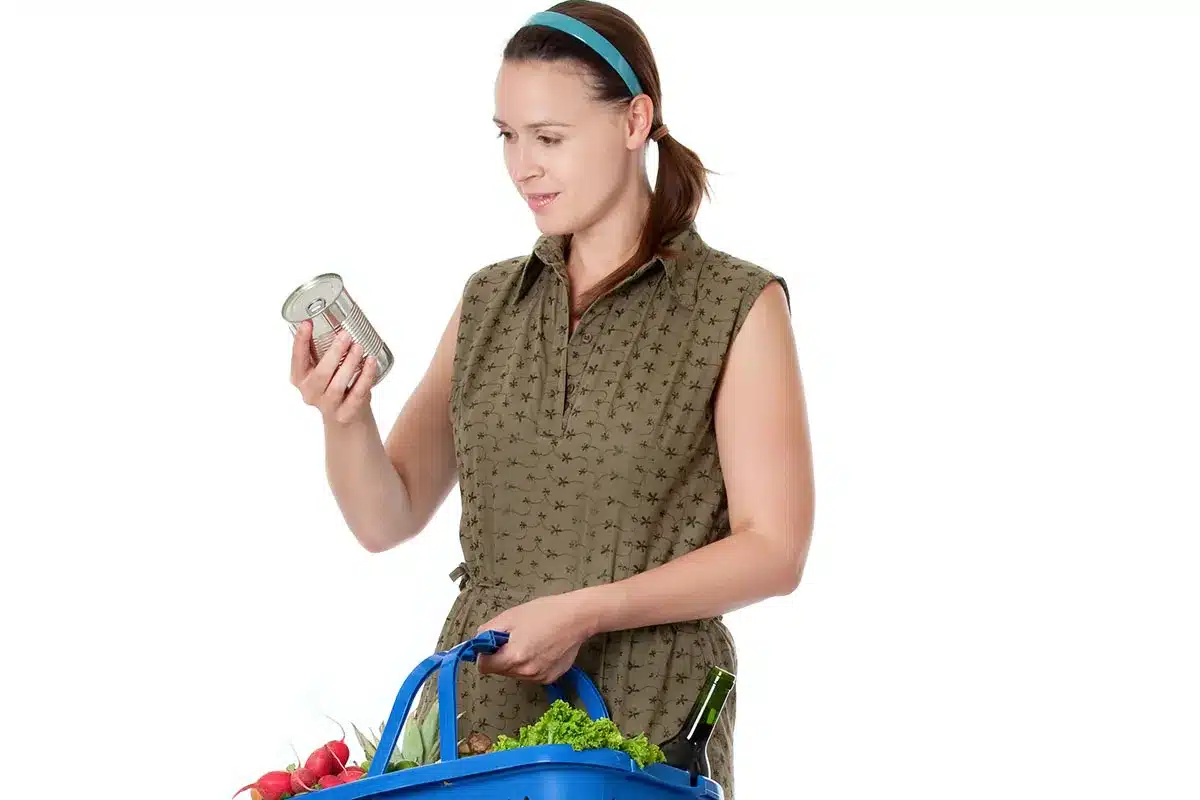 Woman checking a can of food in her shopping basket.