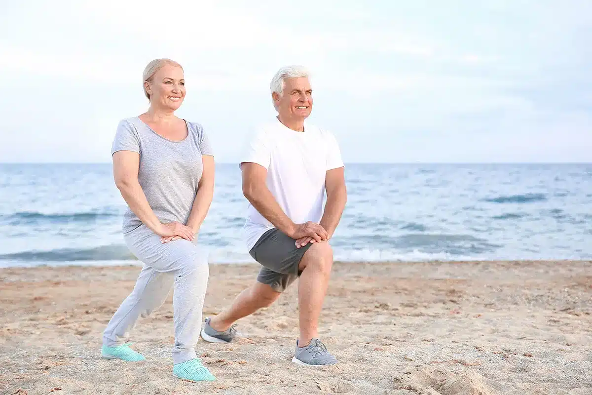 Senior couple stretching on the beach.