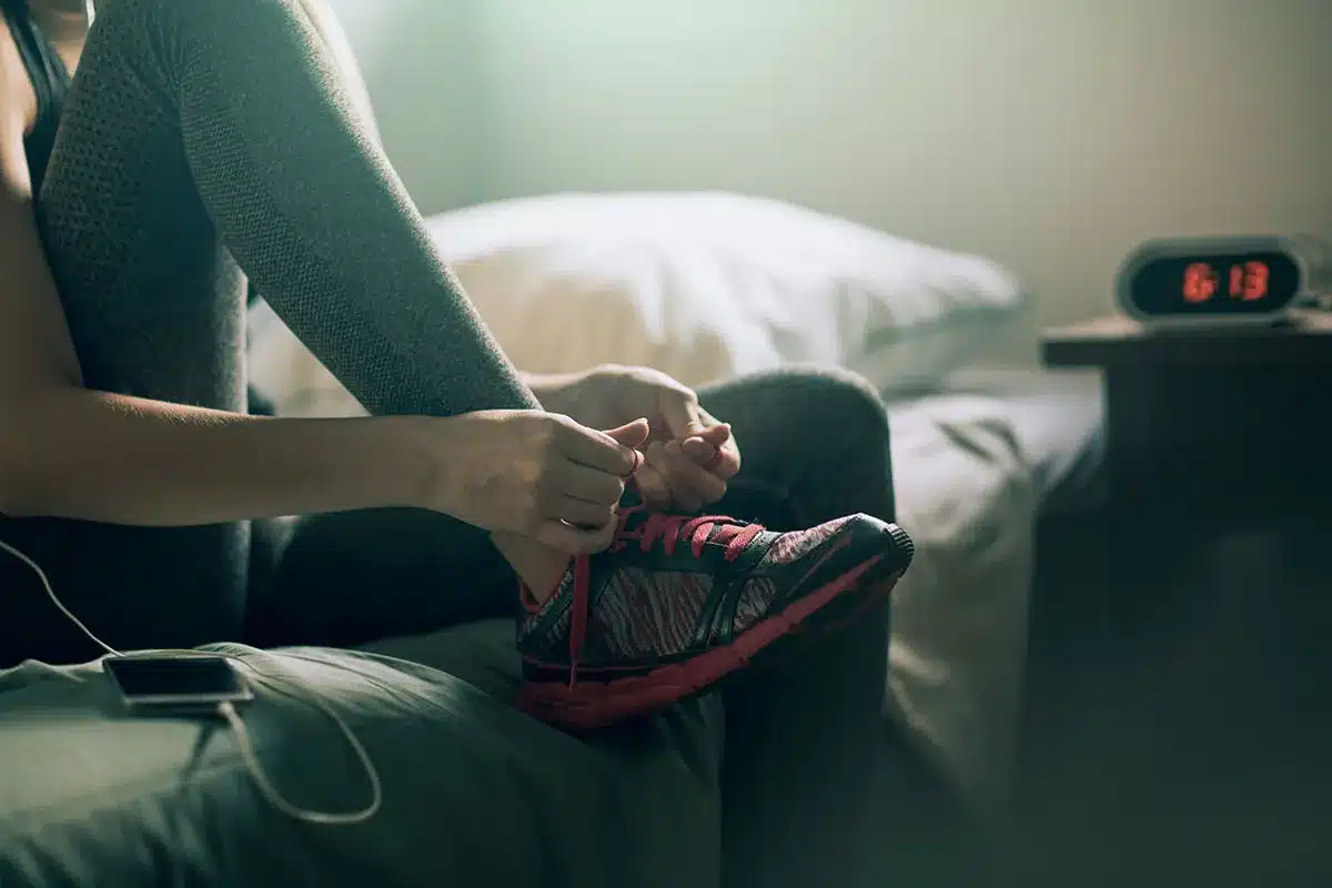 Woman tying running shoes on bed.