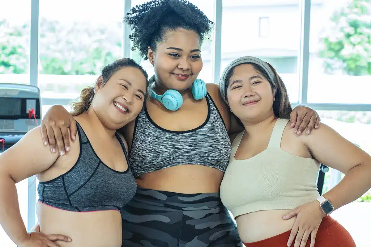 Three plus-size women smiling at the gym.