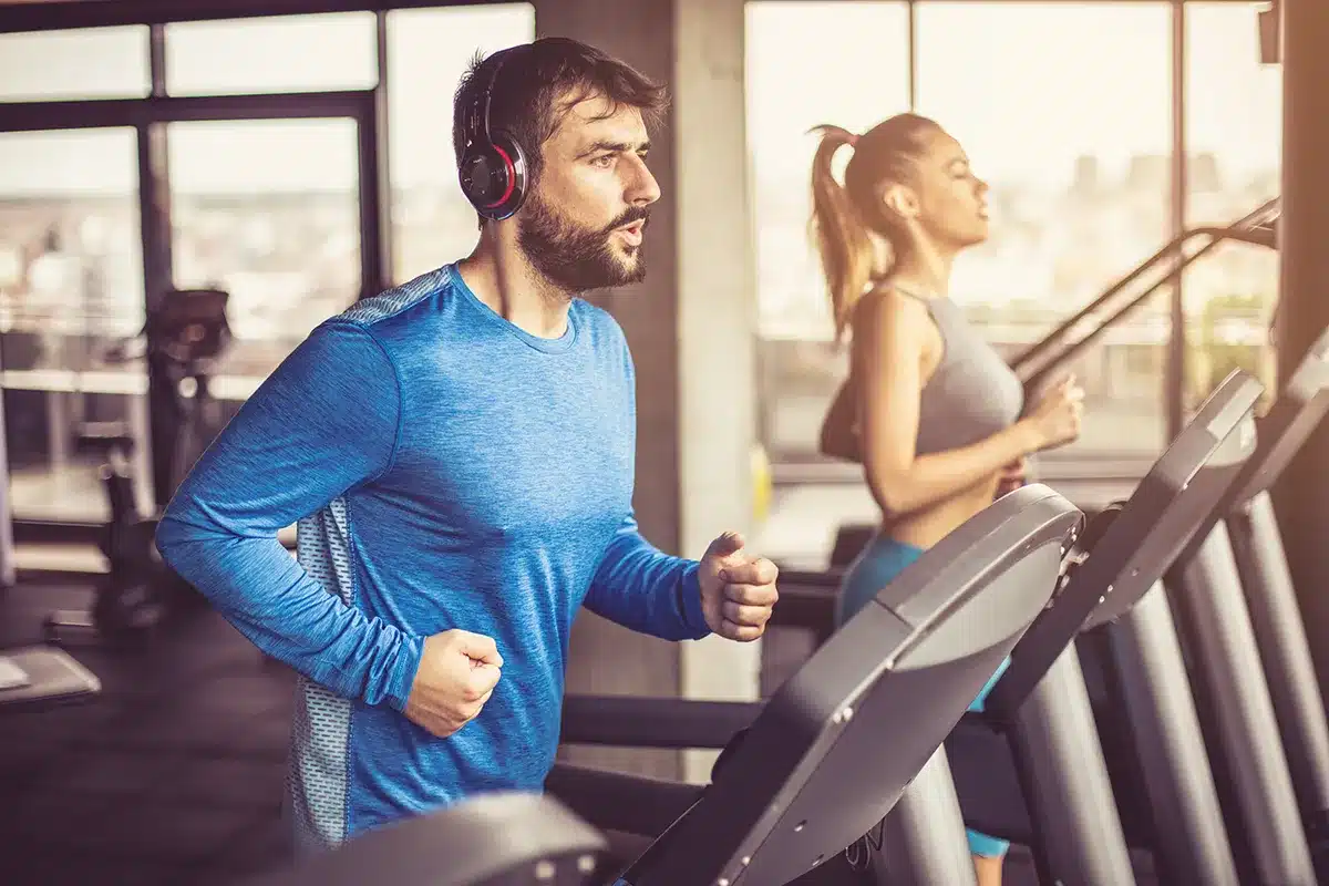 Man and woman running on treadmills at gym.