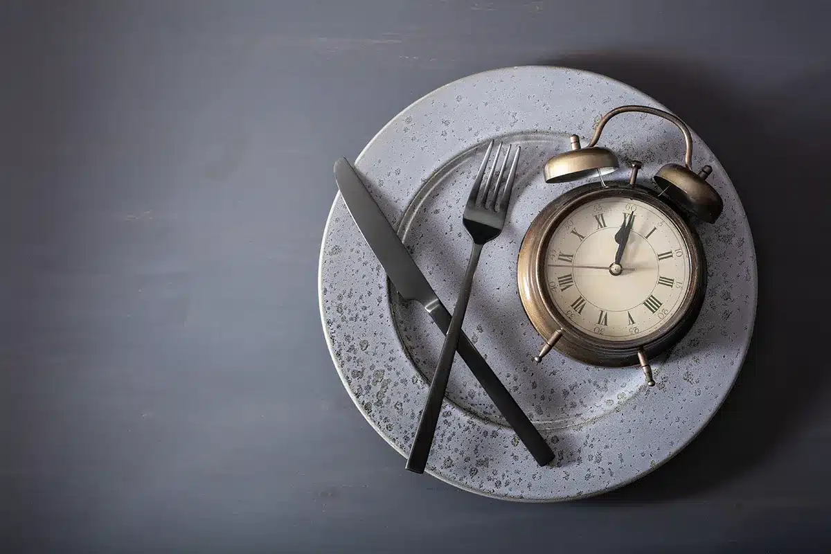 An alarm clock showing midnight sits on a plate with a knife and fork.