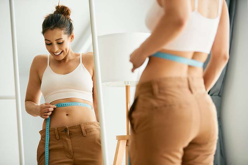 happy woman measures her slim waist with tape measure