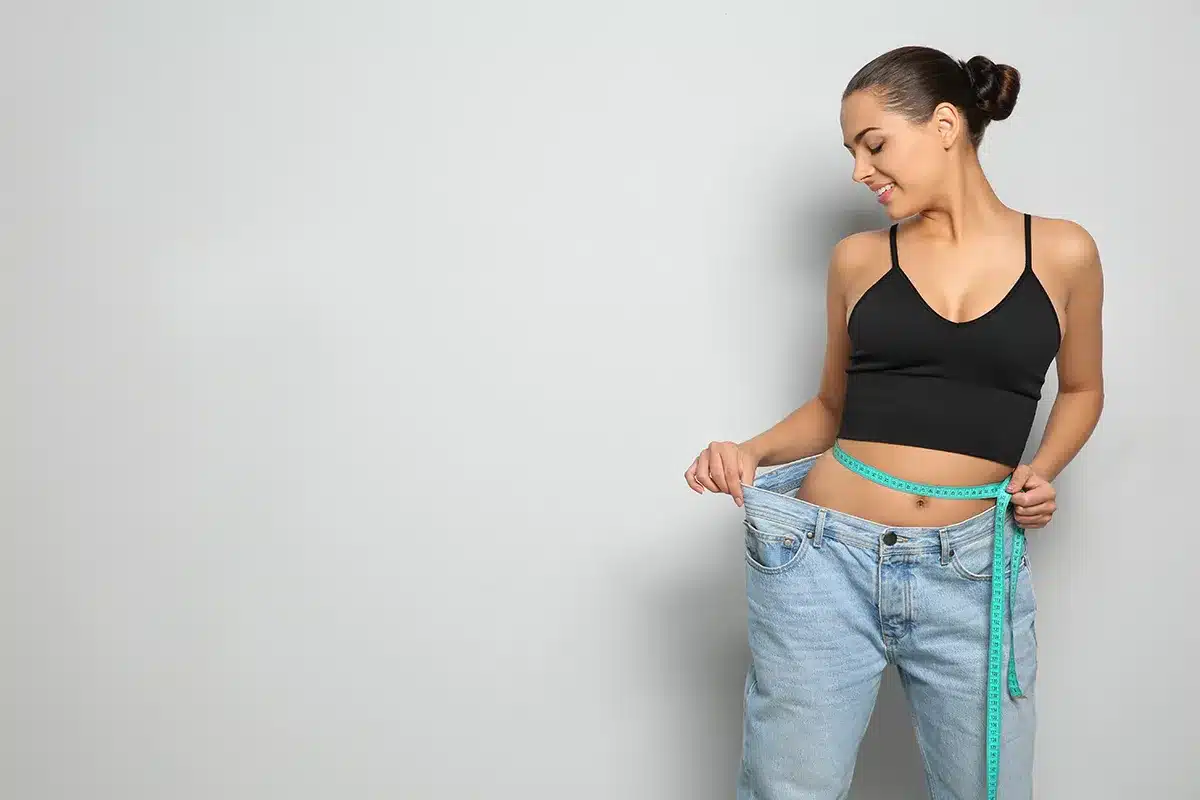 Woman showing weight loss, holding large jeans.