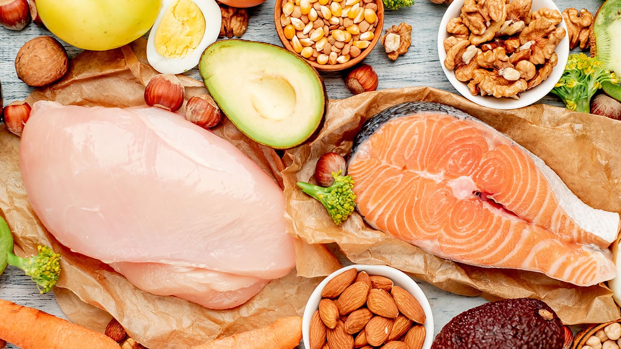 Fresh healthy foods: chicken, salmon, avocado, nuts, eggs, vegetables.