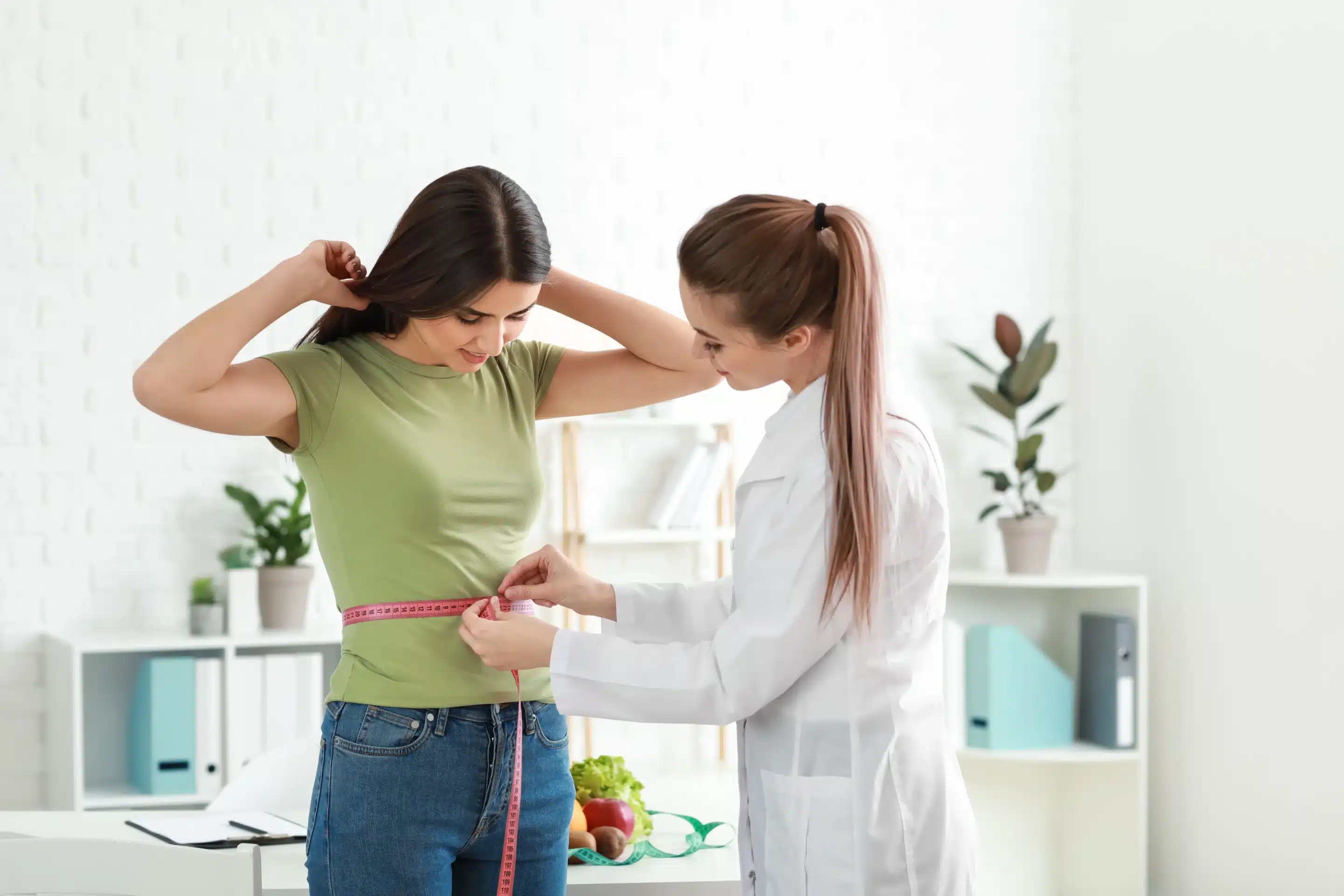 Dietitian using measuring tape to check woman’s waist for weight loss program results