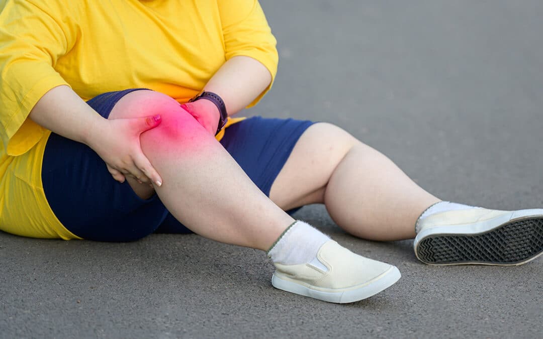 Overweight person sitting on the ground, clutching a knee with highlighted pain.