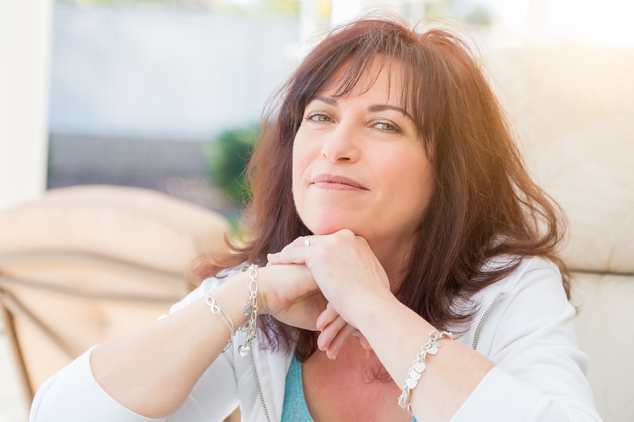 Middle-aged woman with dark hair and green eyes, hands clasped under her chin.