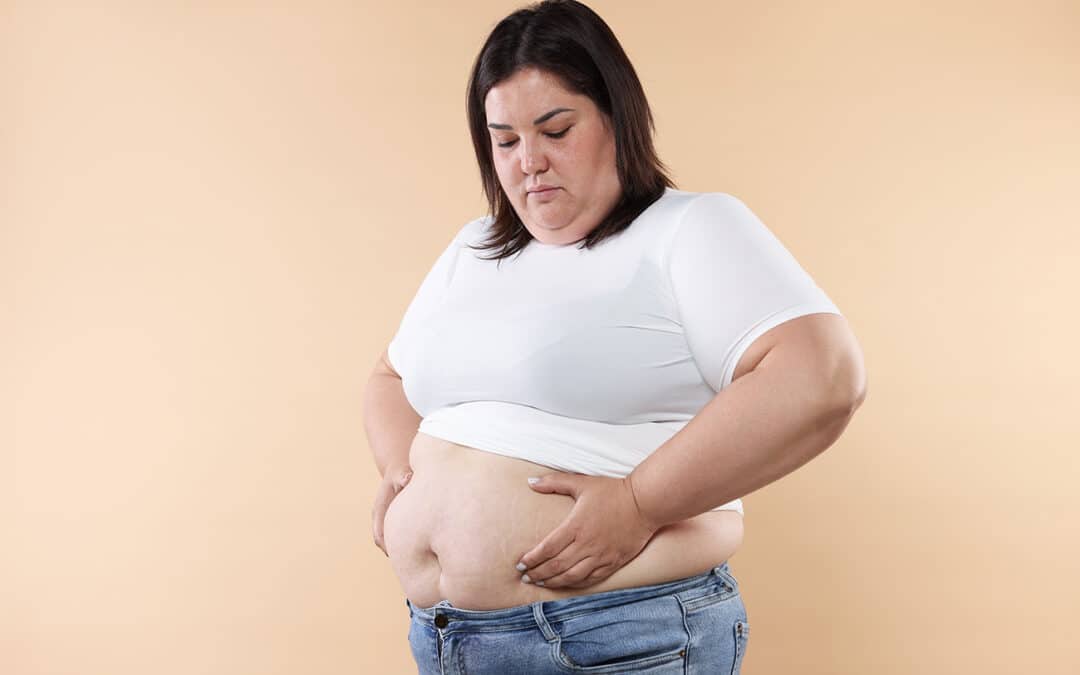 A woman in a white t-shirt and jeans inspects her midsection with a concerned