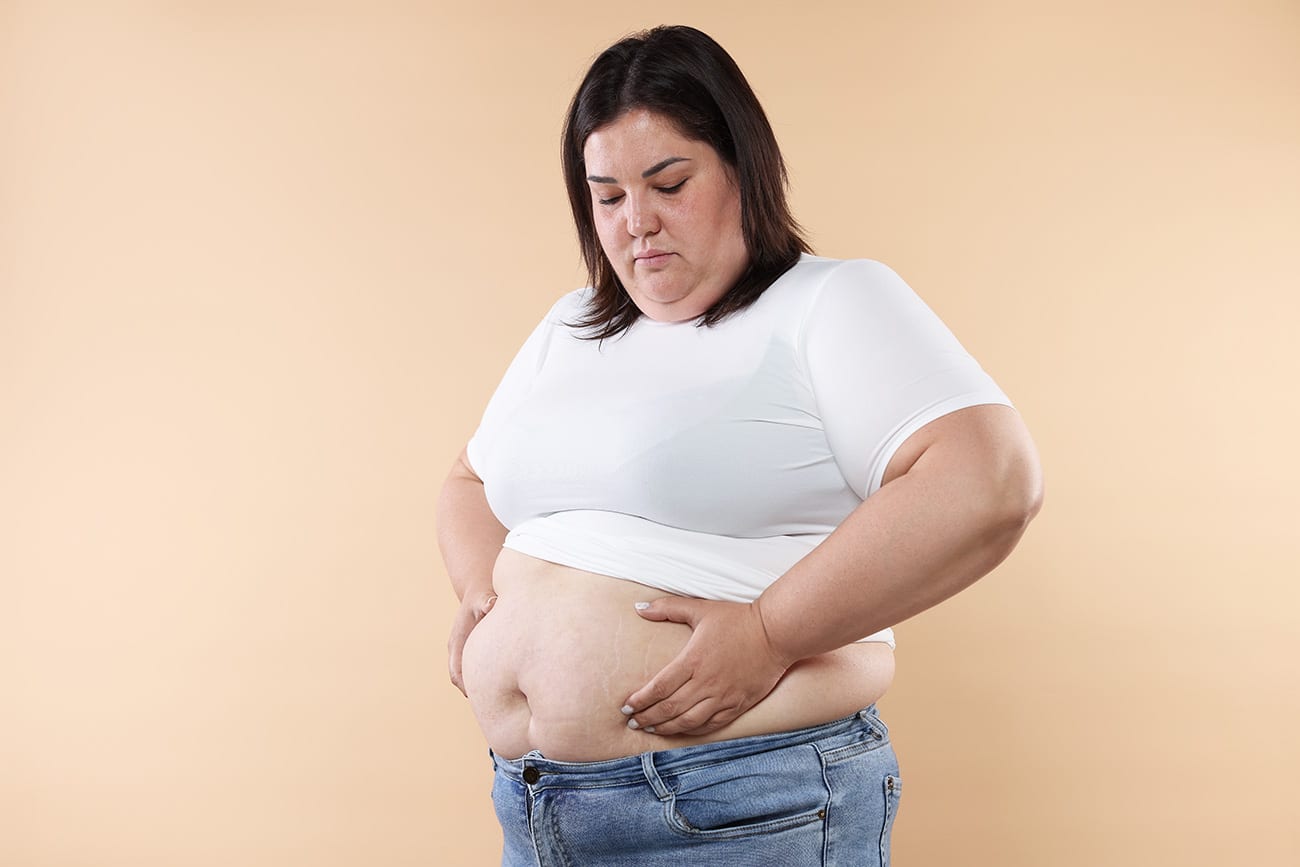 A woman in a white t-shirt and jeans inspects her midsection with a concerned